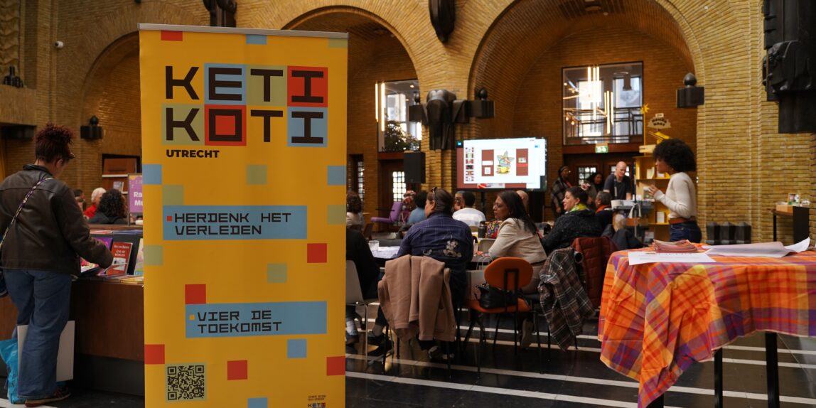 Een kleurrijke banner met Keti Koti erop staat bij de ingang van het event.