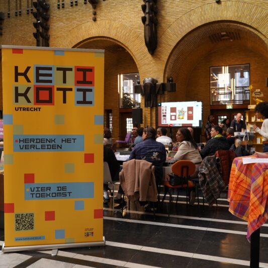 Een kleurrijke banner met Keti Koti erop staat bij de ingang van het event.